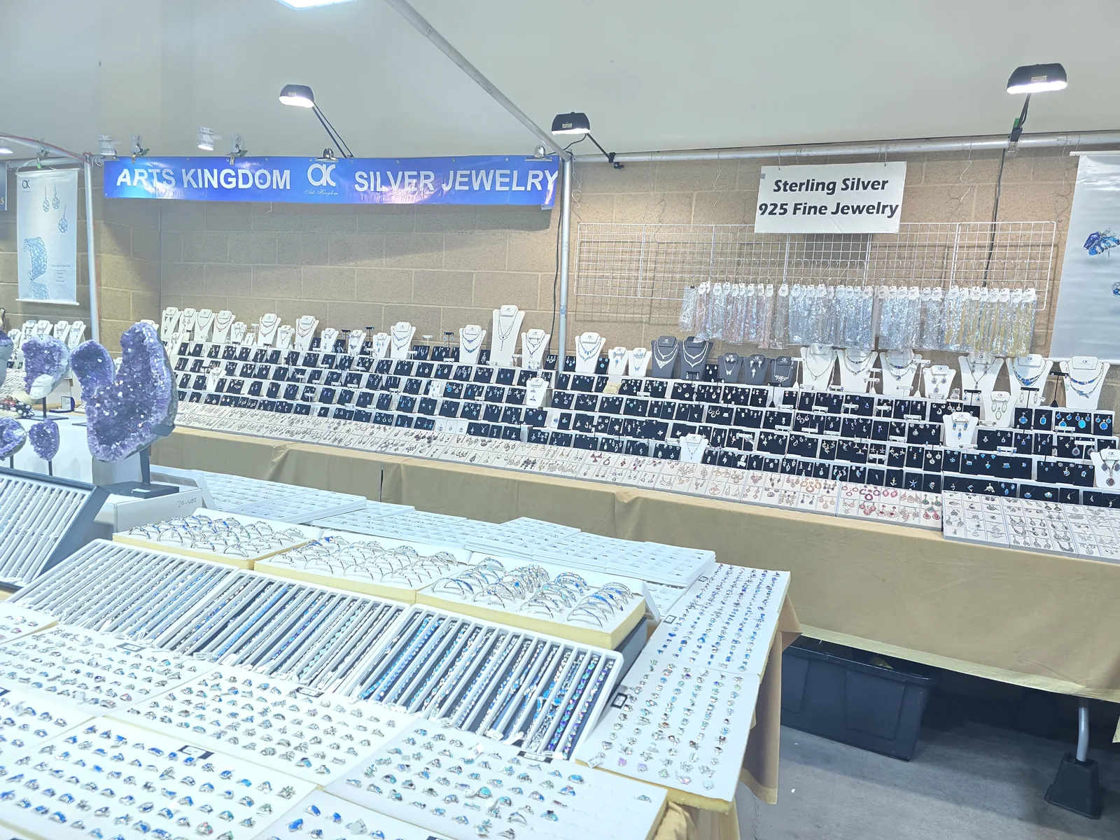 Arts Kingdom Silver Jewelry 展位,蓝色横幅与 Sterling Silver 925 Fine Jewelry 立牌,后墙整排银饰挂卡,前排白色托盘装满上千枚银戒指