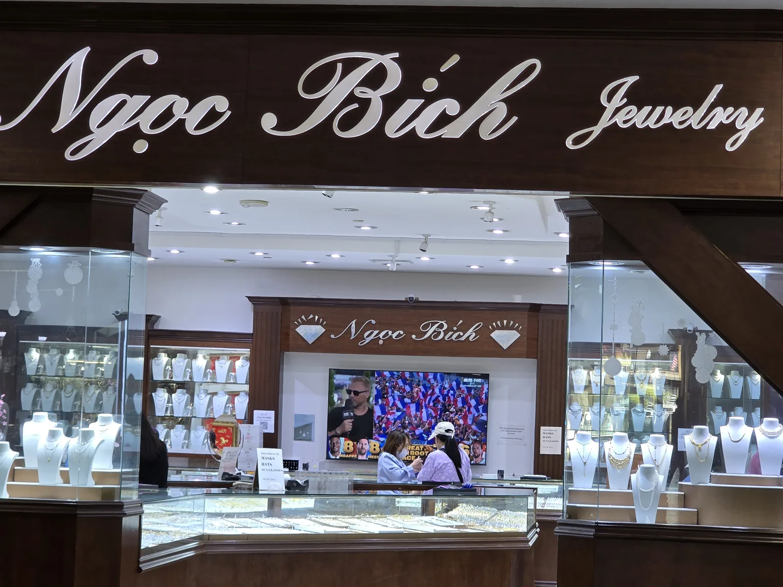 Ngoc Bich Jewelry 柜台,银字花体招牌,金链与珍珠陈列,柜台后有电视