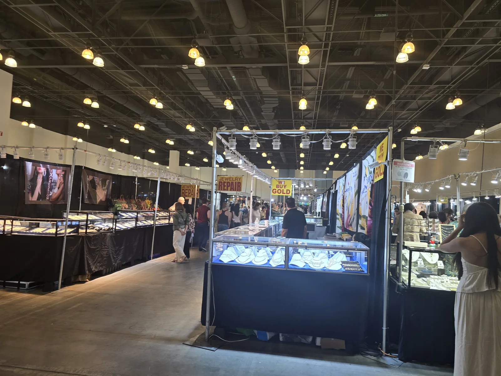 InterGem 展会较高端成品珠宝通道,两侧黑色玻璃柜内灯打亮,顾客走动