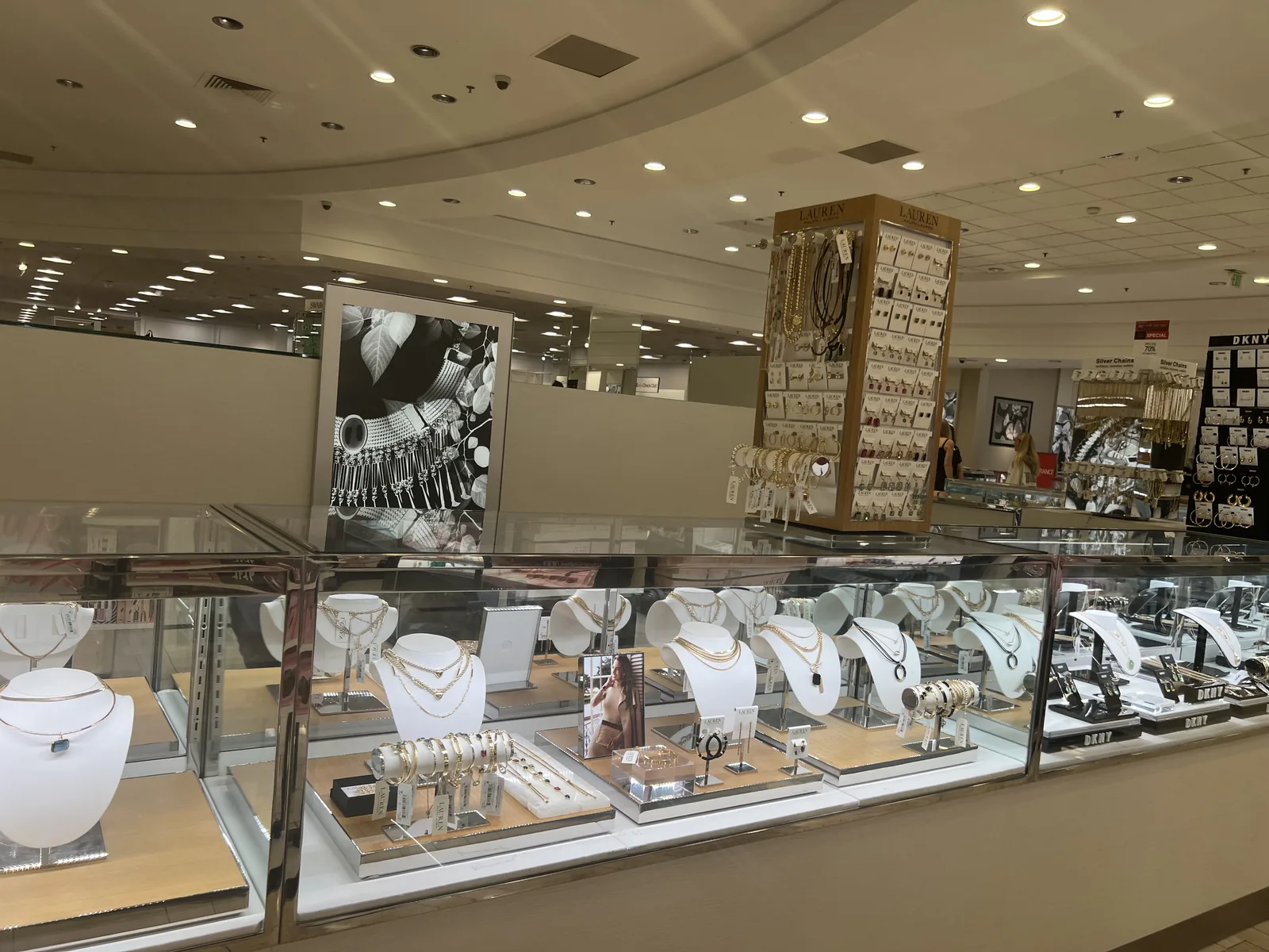 Macy's 珠宝层,Lauren Ralph Lauren 旋转架、DKNY 墙与银链区,挂着 70% off 促销牌