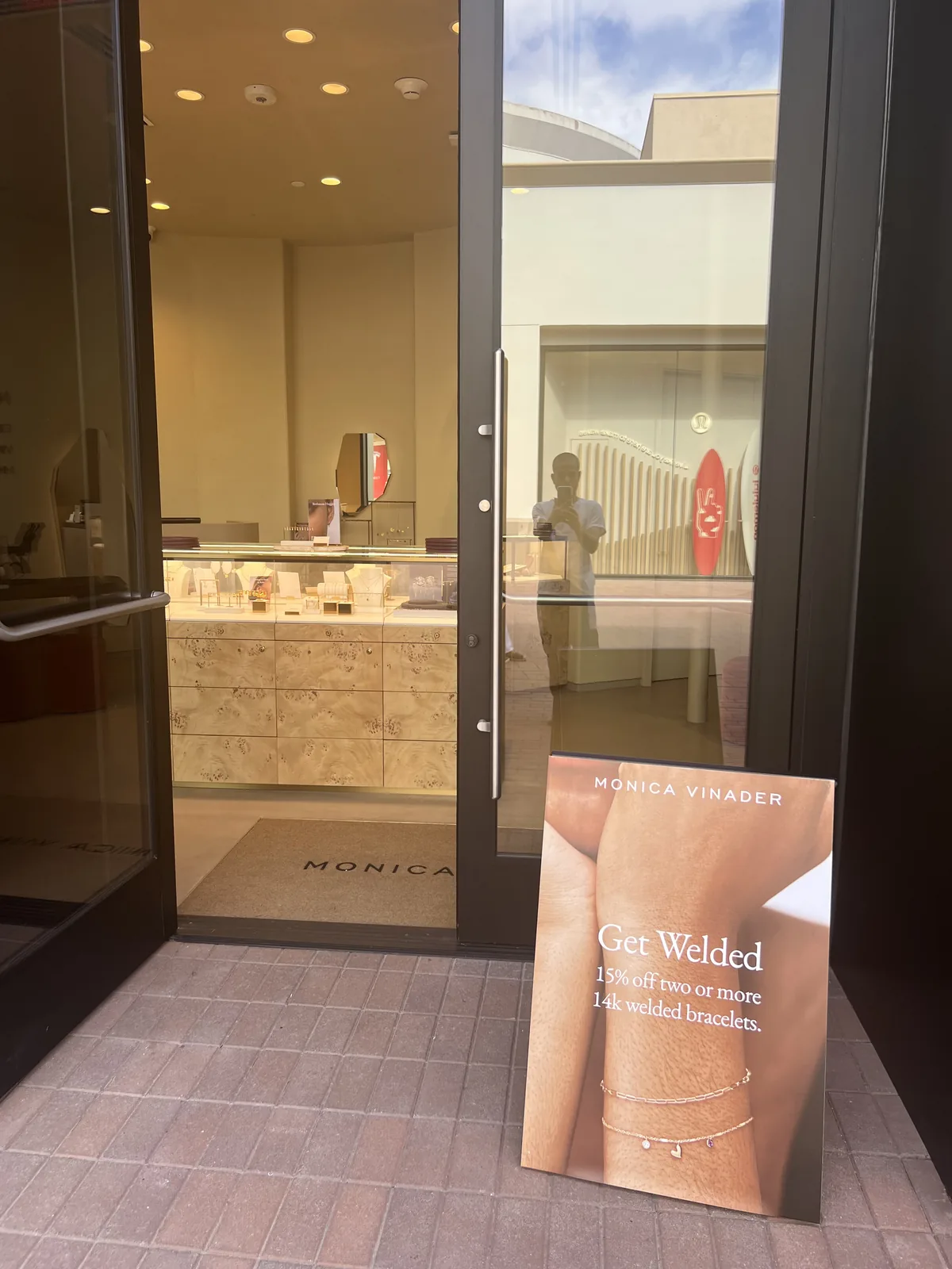 Monica Vinader 店门口的 Get Welded 永久焊接手链促销 A 字牌,店内是原木饰面柜台